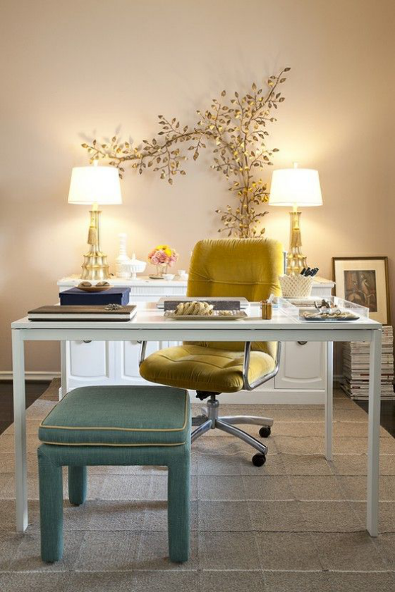 Home Office Design Ideen sehr stilvoll zwei Lampen dazwischen goldene Blätter als Deko gelber Sessel grüner Hocker weißer Schreibtisch