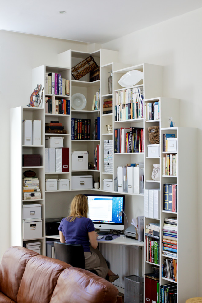 Kleines Home Office in der Ecke des Wohnzimmers Regale viele Ordner Dokumente Bücher junge Frau vor dem PC