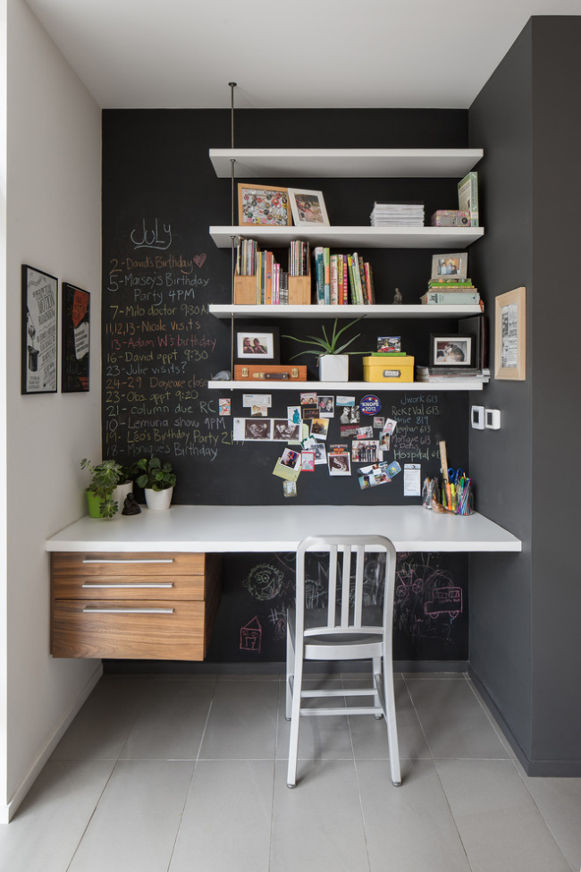 Kleines Home Office in der Raumnische schwarze Wand rechts weiße Wand links schwarze Tafel Notizen weißes Regal Bücher viele Fotos