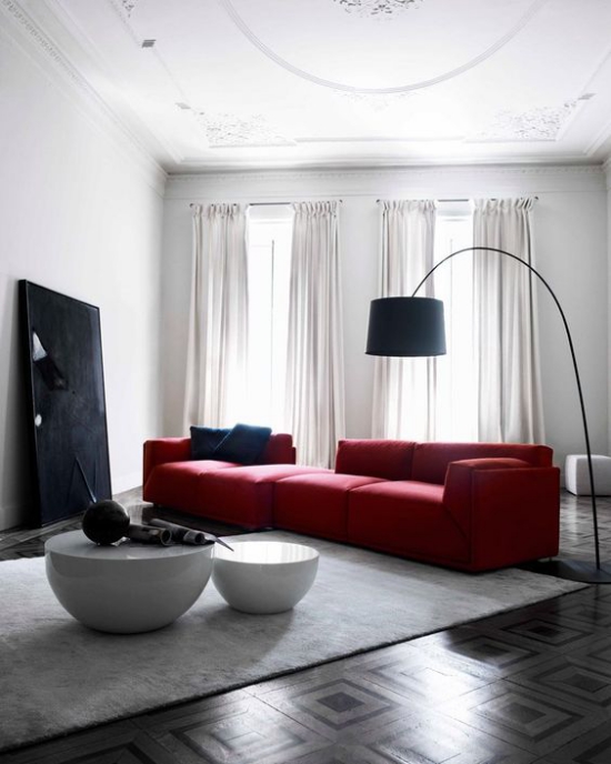 Rotes Sofa Raffinesse im Interieur hellgrauer Teppich Bogenlampe kleine runde Tische weiße Wände Gardinen