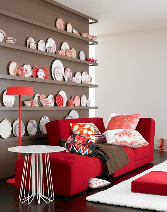 Rotes Sofa Regalwand verschiedene weiße und rote Teller rote Stehlampe weißer Teppich weißer Tisch