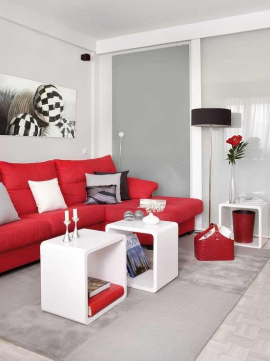 Rotes Sofa kleine weiße Tisch modernes Raumdesign hellgrauer Teppich Wandbilder weiße Kerzen