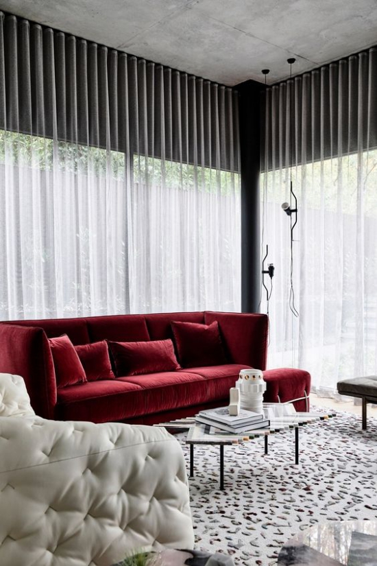 Rotes Sofa vor dem Fenster platziert schönes Raumdesign weißer Sessel Gardinen Teppich wenig gemustert