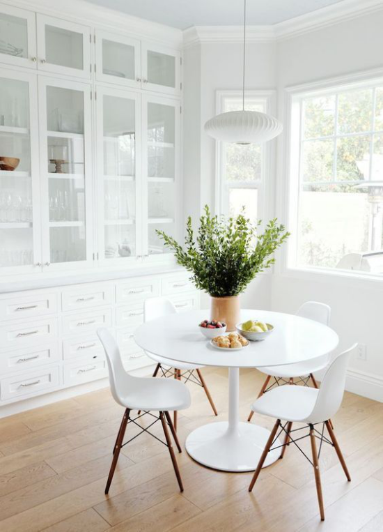 Esszimmer in neutralen Farben viel Weiß heller Holzboden kleiner runder Esstisch vier weiße Stühle Vase mit grünen Zweigen