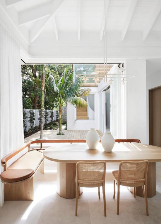 Esszimmer in neutralen Farben viel Weiß und helles Holz elegante Esszimmermöbel gepolsterte Sitzbank zwei weiße Vasen schöner Blick zum Innenhof