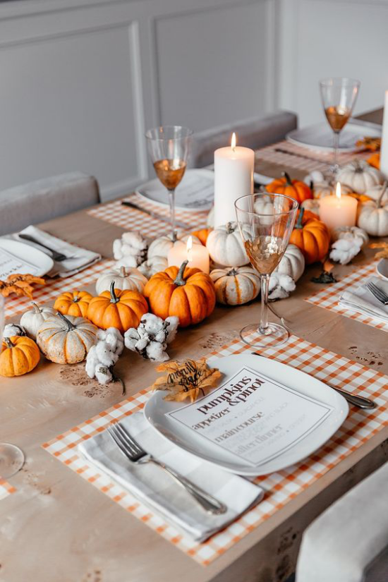 Herbstdeko auf dem Esstisch Herbstzeit ist Kurbiszeit weise und orangefarbene Kurbisse in der Tischmitte arrangiert schickes Geschirr weise Kerzen halbgefullte Weinglaser