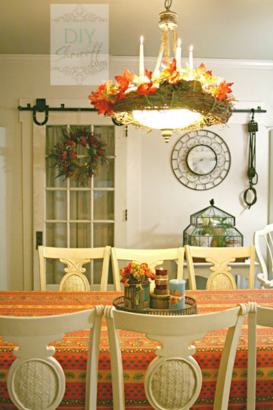 Herbstdeko auf dem Esstisch Kronleuchter herbstlich schmucken mit Blumen und Laub bunte Tischdecke Orange dominiert Vase mit Herbstblumen