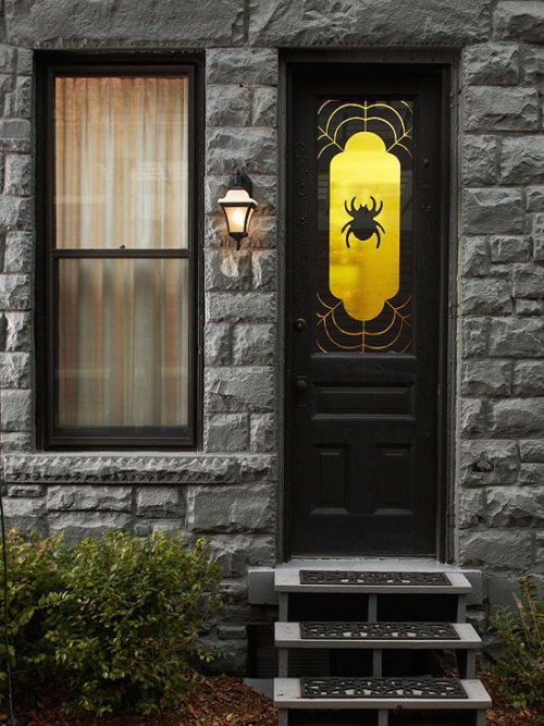 Halloween Deko vor der Haustur stilvoll gestaltet grose Spinne an der Fensterglasscheibe in Gelb beleuchtet drausen Wandlaterne