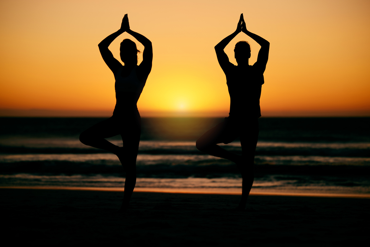 Zwei Menschen praktizieren Yoga am Strand beim Sonnenaufgang
